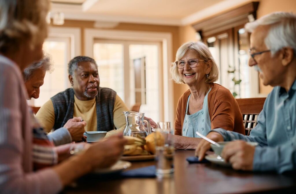 A group of seniors in an assisted living community sitting around a table, eating and enjoying breakfast while smiling and chatting with each other