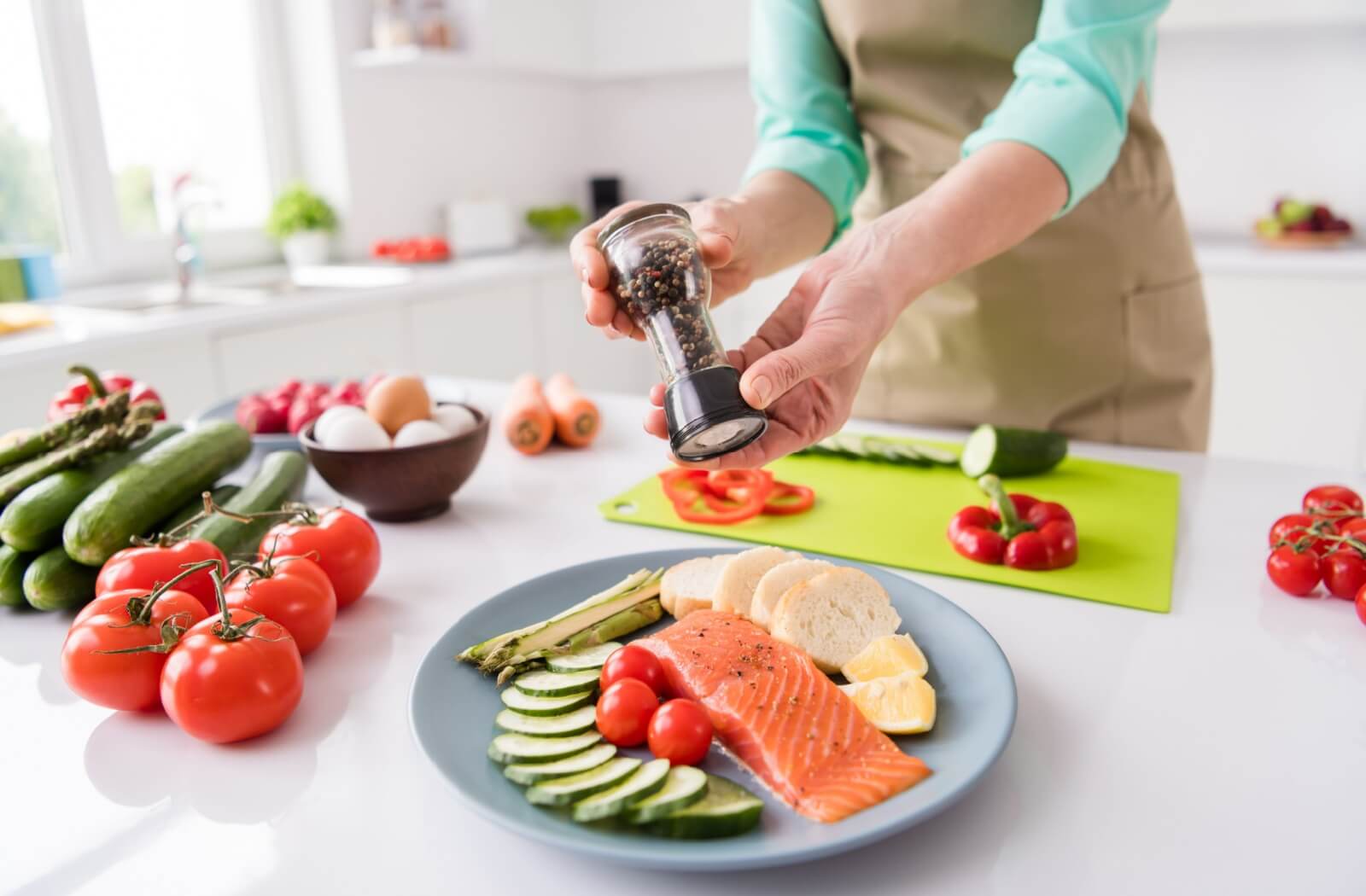 A close-up image of a senior preparing a colorful dish with salmon and lots of vegetables