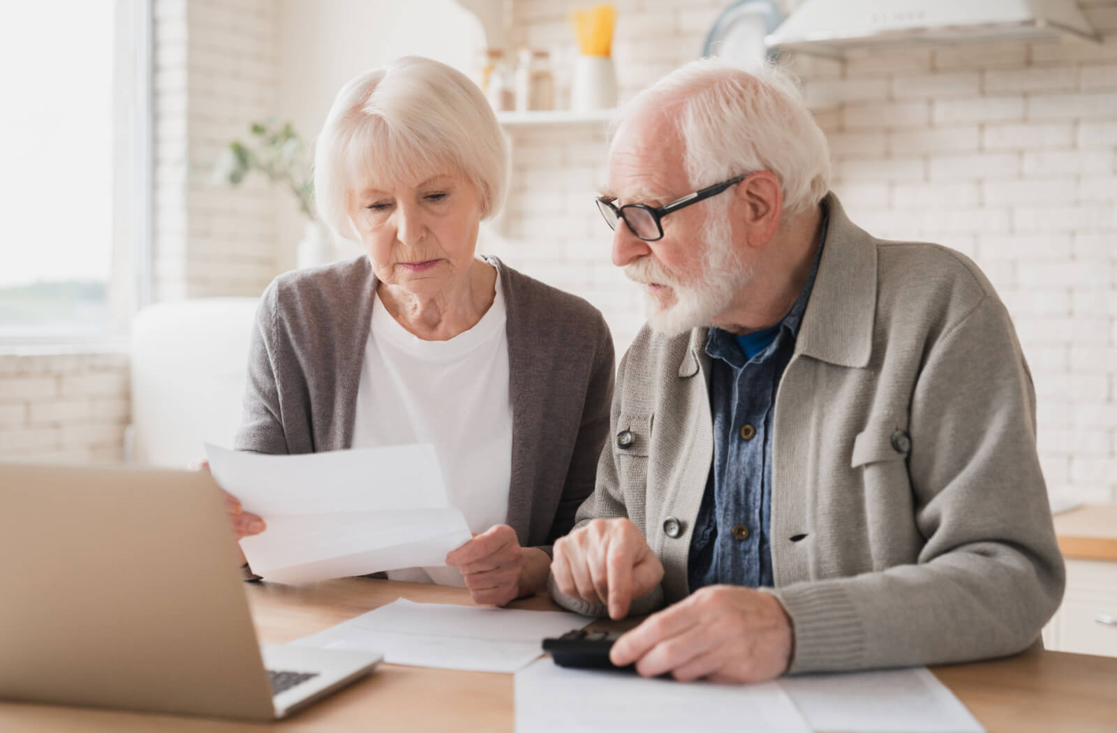 An older couple working together doing paperwork in their kitchen to understand the costs of living in senior living.