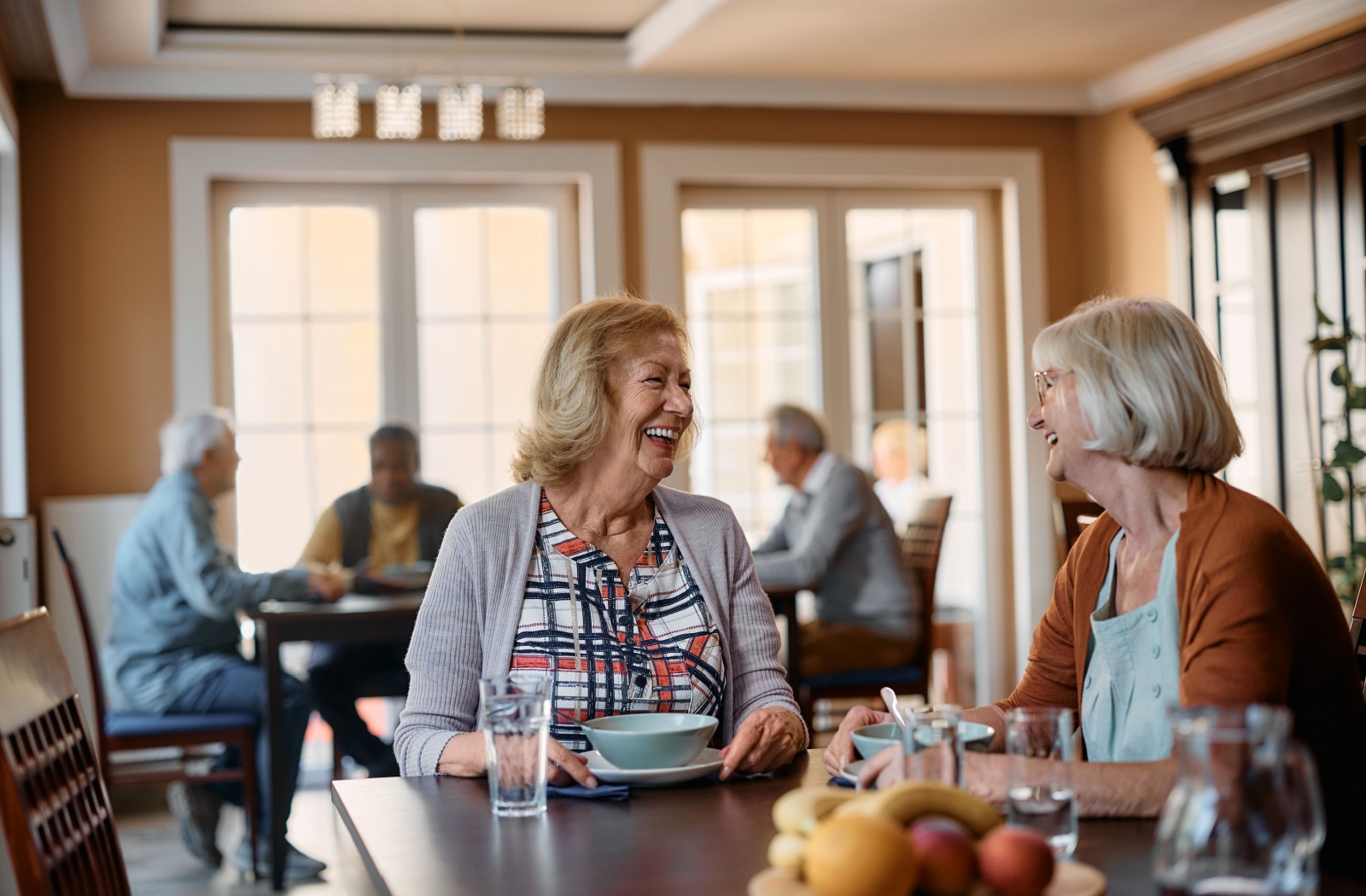 A couple of seniors laugh and enjoy a meal together in their assisted living communal dining area.