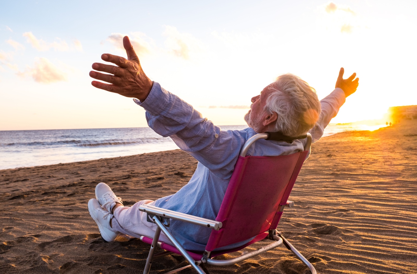 An older adult stretches out their arms as they enjoy an evening on the beach
