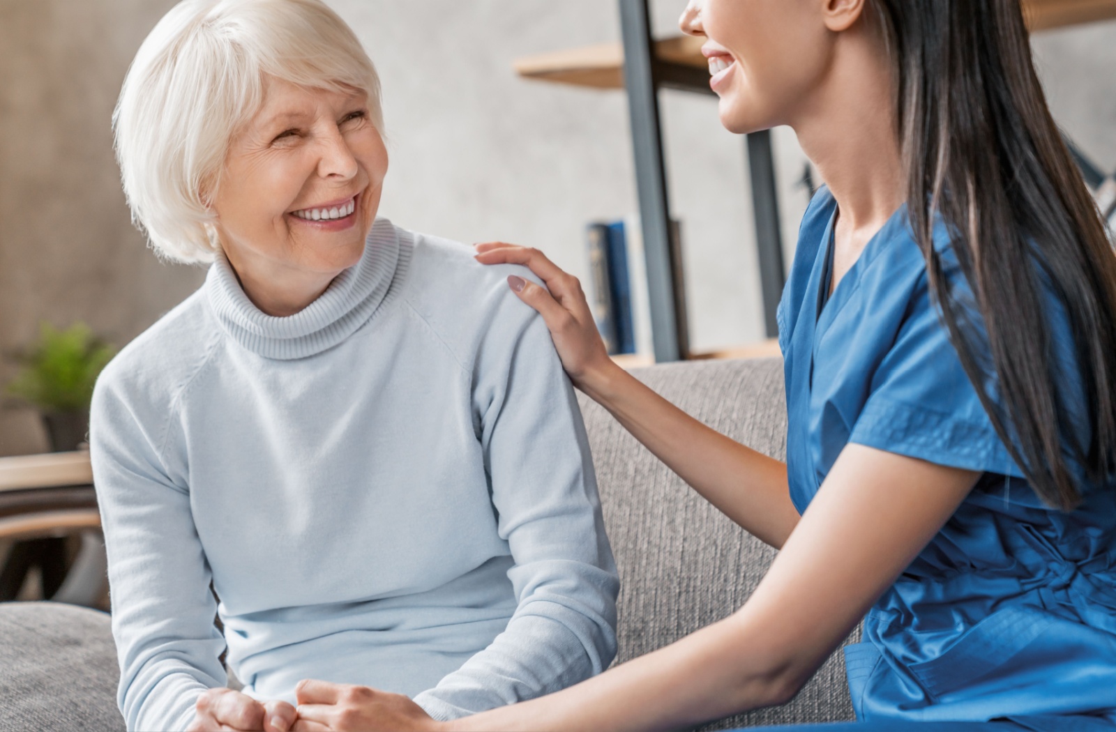 A caregiver checking in on a happy resident in memory care, sitting together on the couch.