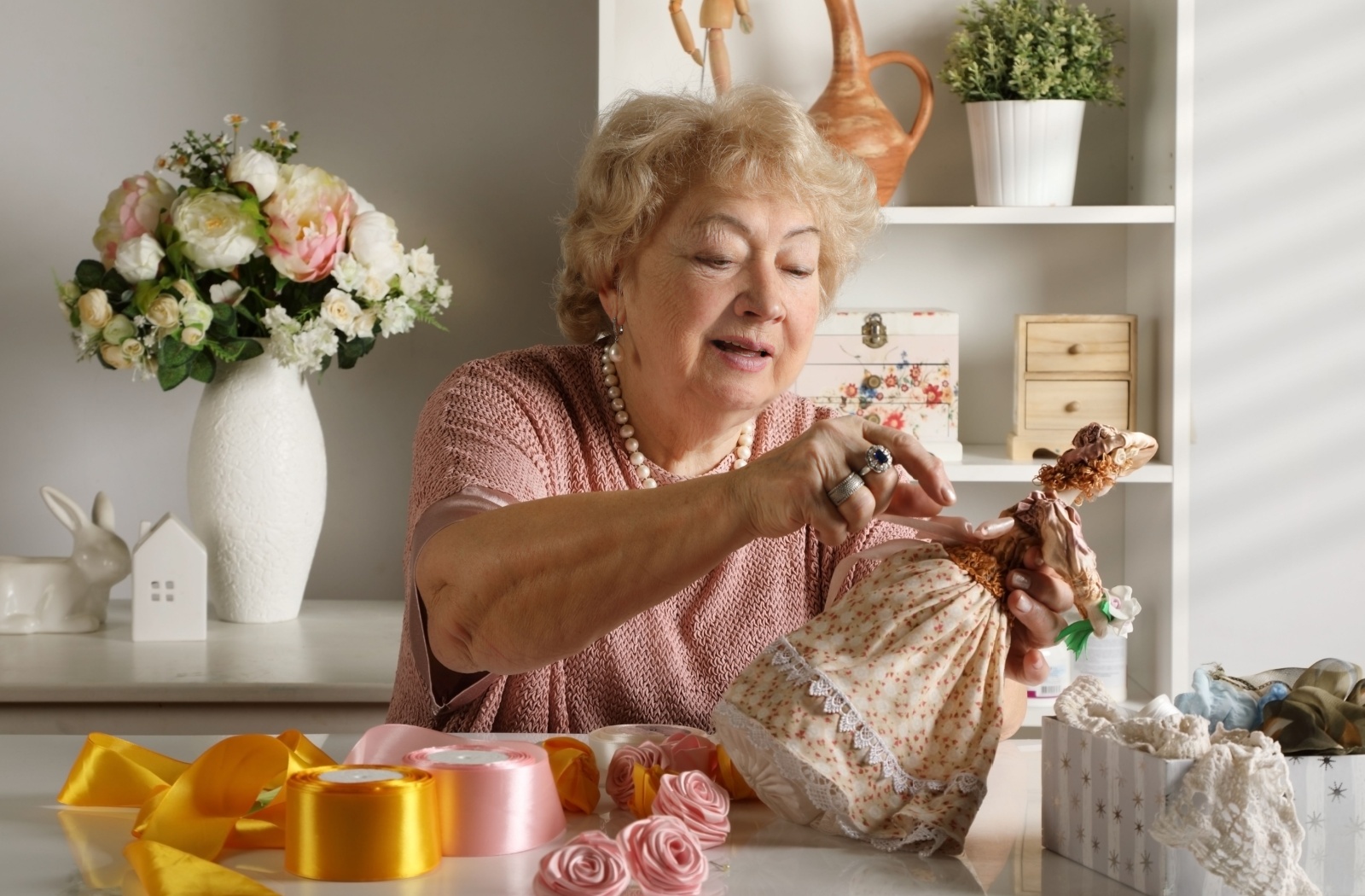 Senior creating a handmade doll with ribbons and fabric surrounded by colorful craft supplies on a table