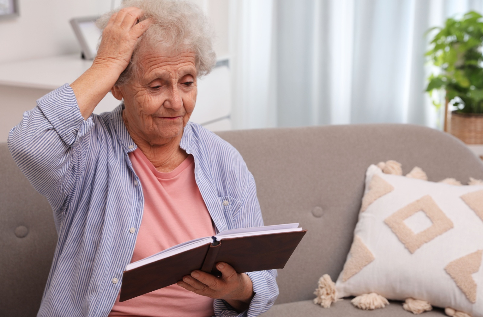 An older adult touches their head while reading a journal, feeling overwhelmed by memory loss.