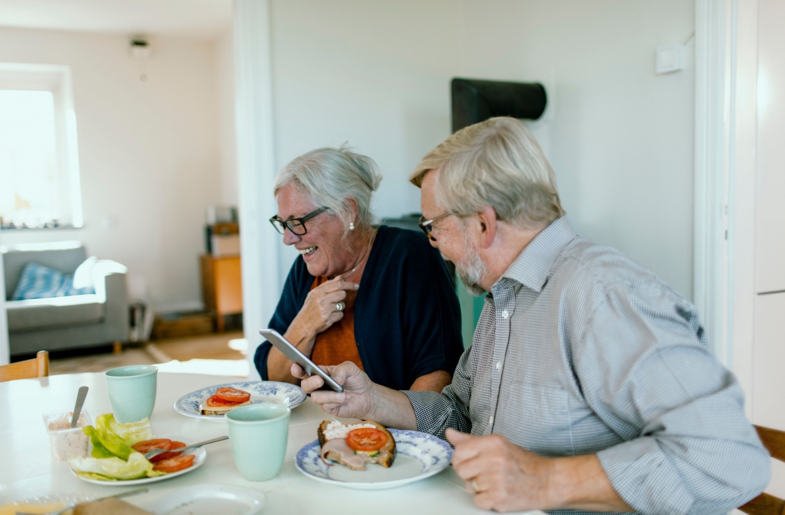 A senior couple laugh as they share a meal together.
