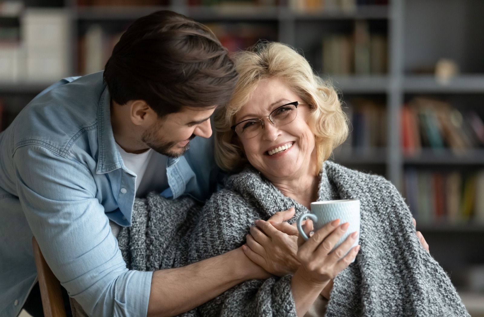An adult child embraces their smiling senior parent with dementia